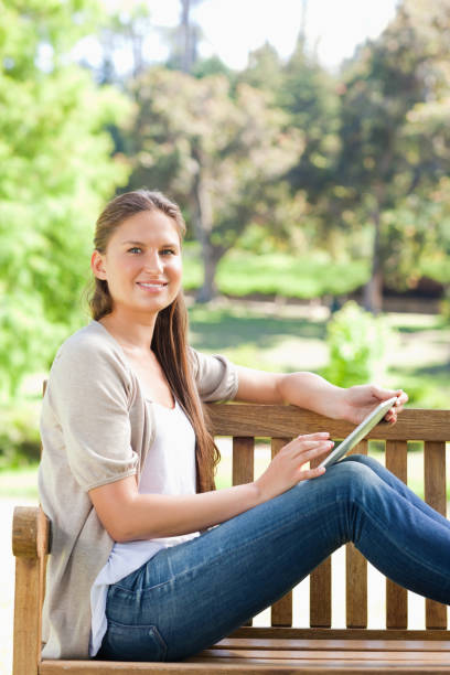istock Side view of a smiling woman with a tablet computer on a park bench 842153426