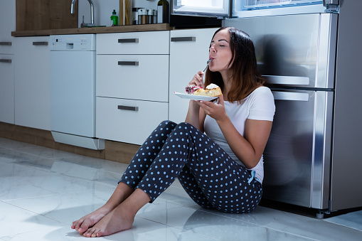 Young Woman Enjoy Eating Sweet Food While Sitting On Floor In Kitchen