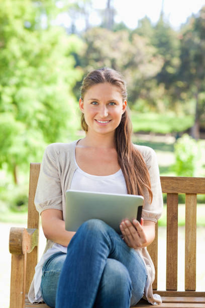 istock Smiling woman on a park bench with a tablet computer 842163856