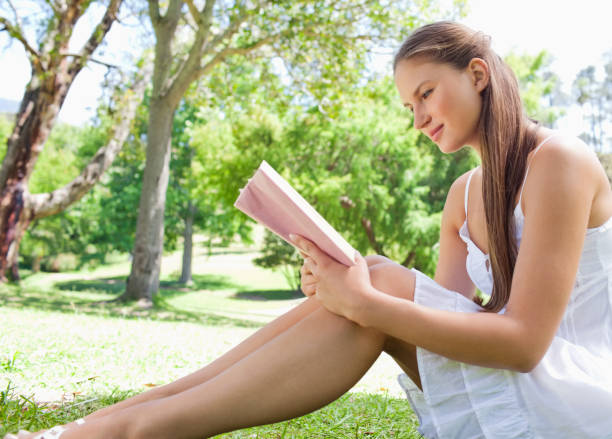istock Side view of a woman sitting on the lawn while reading a book 842174016