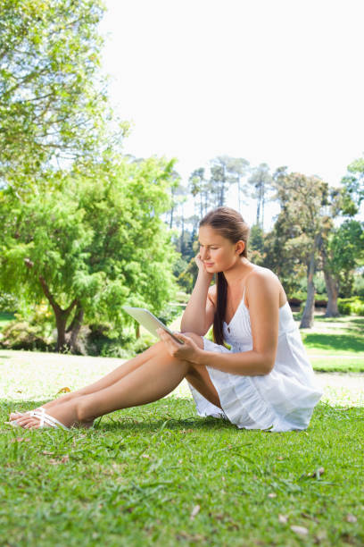 istock Side view of a woman with her tablet computer sitting on the lawn 842174208