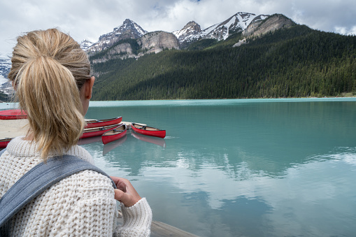 Rear view of a young woman standing by a mountain lake, Lake Louise, Banff national park, Canada. 