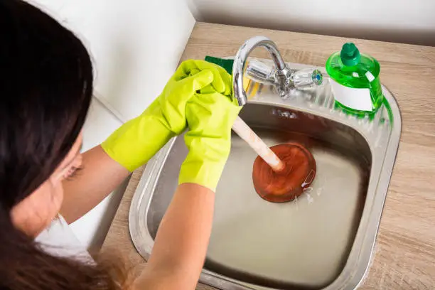 Close-up Of Person Using Plunger In The Kitchen Sink