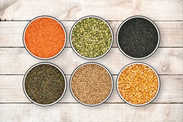Photo of Six lentil bowls on wood background from directly above