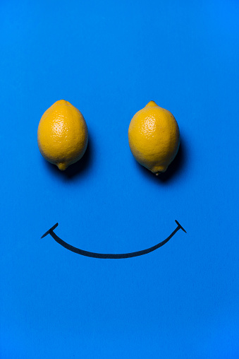 Happy face made with two lemons and smile drawn on blue background