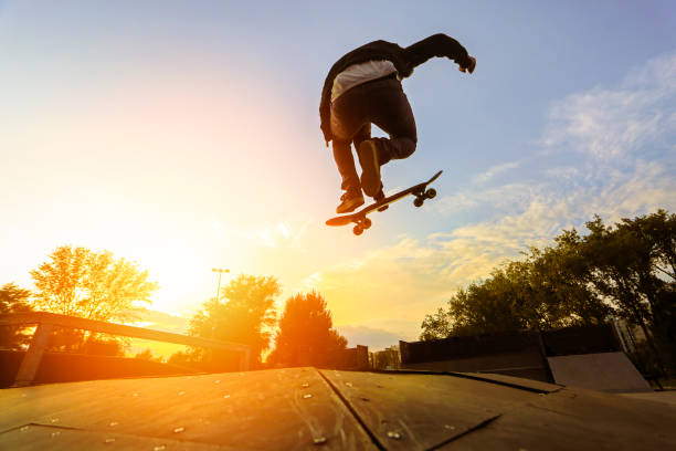 Skater doing a stunt Silhouette of a young skater jumping with skateboard at a skate park at sunset. About 25 years old, Caucasian male."n skateboarding stock pictures, royalty-free photos & images