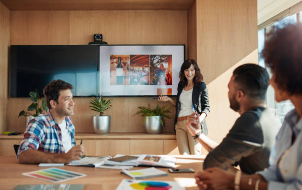Female coworker making presentation in office Female coworker making presentation during business meeting in office. Group of creative designers discussing new marketing ideas together in boardroom. advertisement stock pictures, royalty-free photos & images