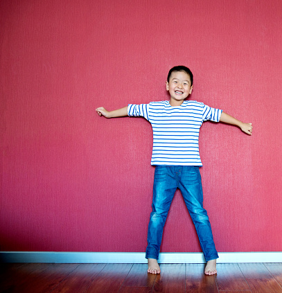 Excited little boy standing against wall with arms outstretched.