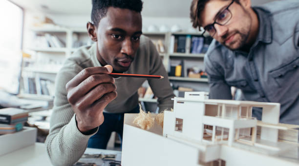 Male architects in office discussing construction project Two male architects in office discussing construction project. Young men working together on new building model. architectural model photos stock pictures, royalty-free photos & images