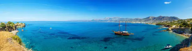 Beautiful scenery - traditional old fashioned cruise boat docked to the sand shore and colorful blue azure crystal clear water of Aegean Sea