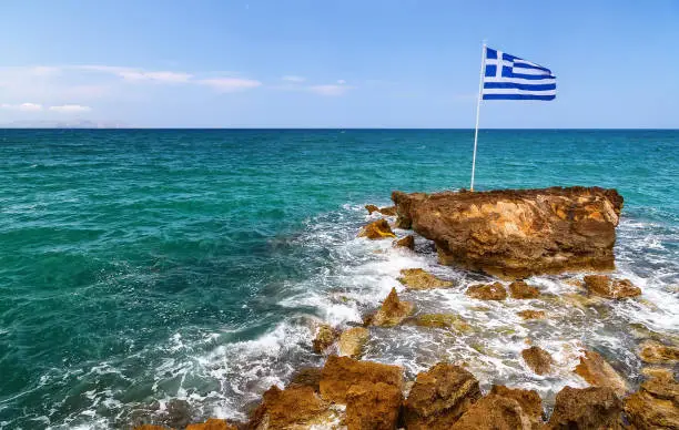 Photo of Greek flag, sea and shore in the background. Crete, Greece