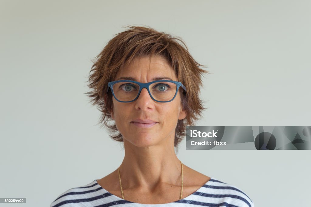 Waist up portrait of adult woman with red hairs, green blue eyes, eyeglasses and cheerful facial expression, in neutral background. Natural soft daylight, natural skin, real people. One Woman Only Stock Photo
