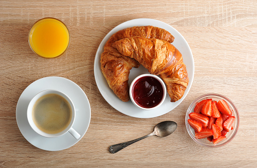 continental Breakfast - coffee, croissant with jam, strawberries and orange juice on wooden background - top view