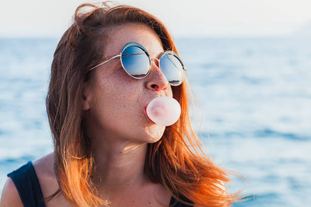 istock Young woman blowing bubble gum by the sea 842276524