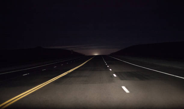 Country Road Dark country road in the Wyoming countryside with the moon just peeking above the horizon. middle of the road stock pictures, royalty-free photos & images