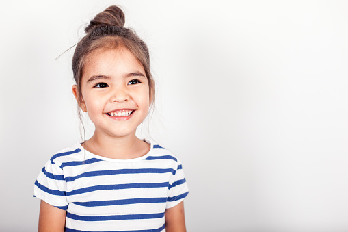 Happy small girl on the grey light background in the studio.