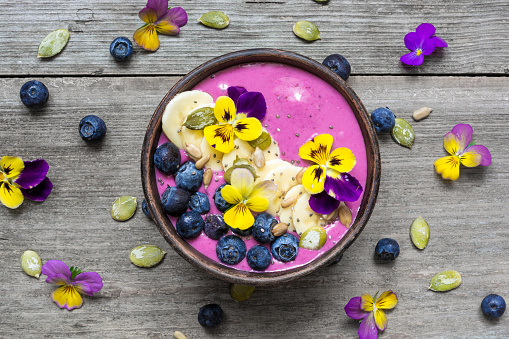 Smoothie bowl with fresh berries, nuts, seeds and flowers for healthy vegan vegetarian diet breakfast. top view