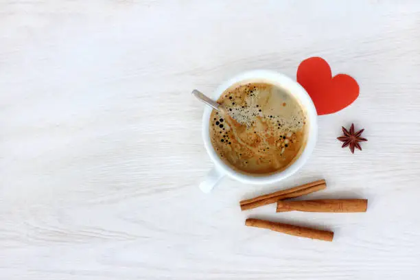 Black frothy espresso with cinnamon and heart symbol on a light wooden table top view