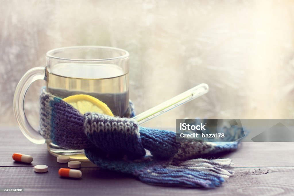 hot drink for convalescence infusion lemon in the transparent mug beside thermometer and tablets on the background of a winter window Cold And Flu Stock Photo