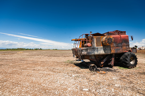 Old burned agriculture combines in a flattened grainfield under a blue sky with white clouds in the countryside of france