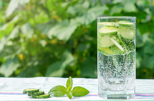 Sliced cucumbers in a glass with mineral water, mint leaves on tablecloths