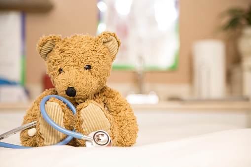 Brown teddy bear and stethoscope on exam table in pediatrician doctor's office.
