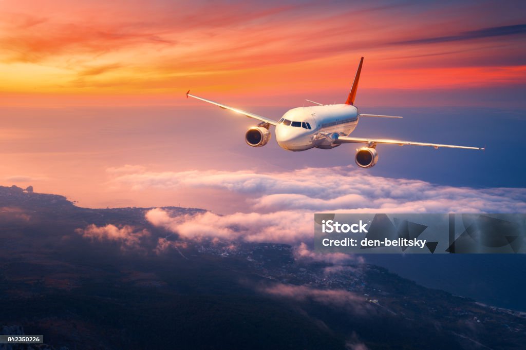 Passenger airplane. Landscape with big white airplane is flying in the sky over the clouds and sea at colorful sunset. Passenger aircraft is landing at dusk. Business trip. Commercial plane. Travel Airplane Stock Photo