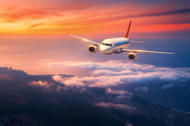 Passenger airplane. Landscape with big white airplane is flying in the sky over the clouds and sea at colorful sunset. Passenger aircraft is landing at dusk. Business trip. Commercial plane. Travel stock photo