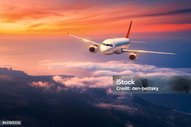 Passenger Airplane Landscape With Big White Airplane Is Flying In The Sky Over The Clouds And Sea At Colorful Sunset Passenger Aircraft Is Landing At Dusk Business Trip Commercial Plane Travel Stock Photo - Download Image Now