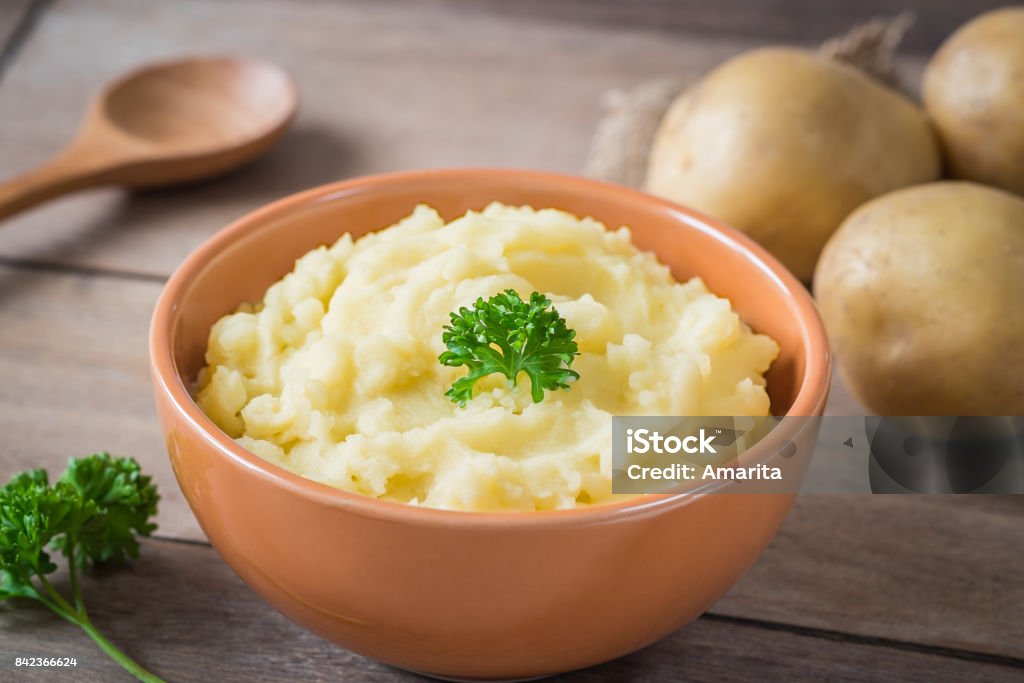 Puré de patatas en el tazón y patatas frescas en la mesa de madera - Foto de stock de Puré de patatas libre de derechos