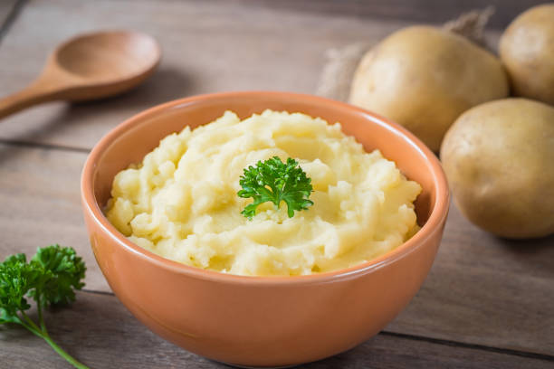 purê de batata na tigela e batatas frescas na mesa de madeira - puré de batata - fotografias e filmes do acervo