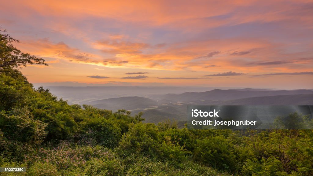 Vivid sunset from Jewell Hollow Overlook in Shenandoah National Park The sun sets and casts a beautiful pink, orange, and yellow glow on the sky as darkness begins to settle over the valley below Shenandoah National Park Stock Photo