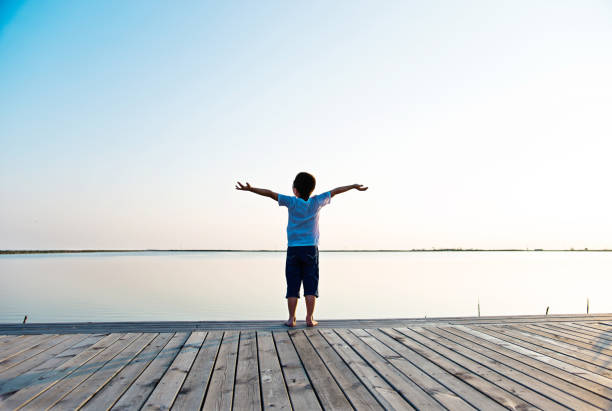 istock Little boy standing at lakeside with arms outstretched 842376350