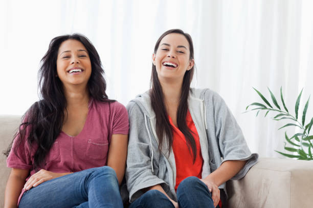 istock Two women sit beside on another on the couch while laughing 842386838