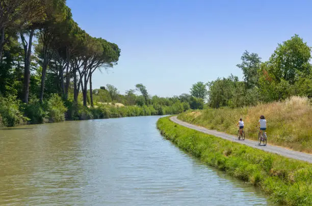Family on bikes, mother and daughter cycling by canal du Midi, active summer vacation in France