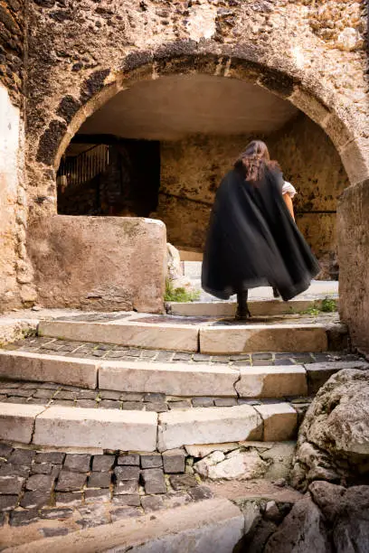 Man with long dark hair wearing a black cape runs up the stone stairs to enter a mysterious ancient sporti, one of nine tunnels in the fortified medieval village of Castel del Monte in Gran Sasso National Park, L'Aquila province, Abruzzo, Italy, Europe
