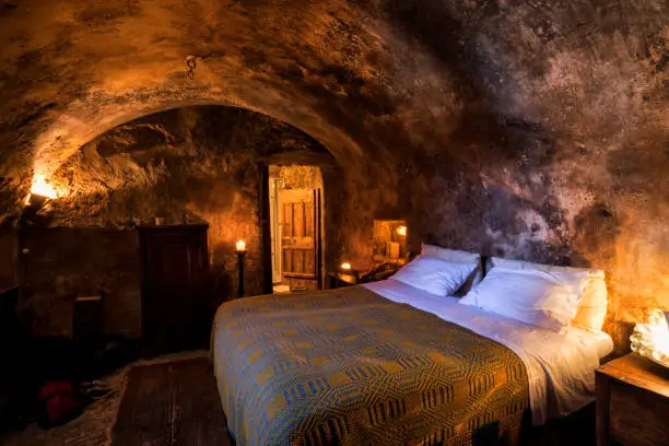 Cave-like medieval guest room with lit candles, massive wooden doors and an arched ceiling in Santo Stefano di Sextantio diffused hotel, Santo Stefano di Sessanio village; Gran Sasso National Park; L'Aquila province, Abruzzo; Italy; Europe
