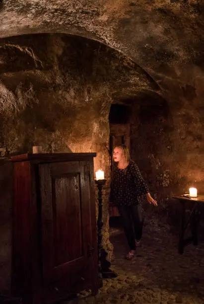 Blond teen looks with excitement at the cave-like medieval guest room with lit candles, massive wooden doors and an arched ceiling in Santo Stefano di Sextantio diffused hotel, Santo Stefano di Sessanio village; Gran Sasso National Park; L'Aquila province, Abruzzo; Italy; Europe