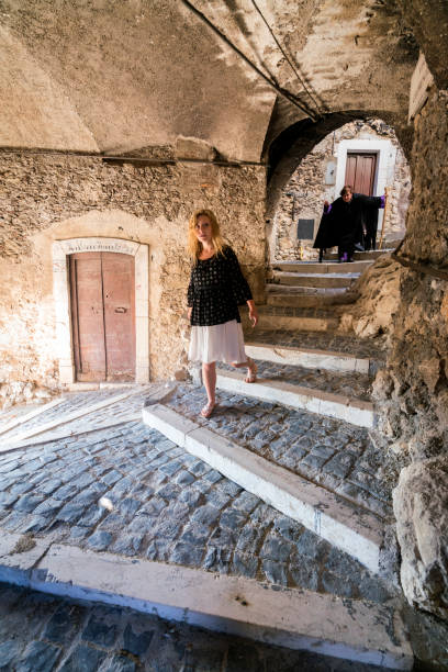 Female witch in a black cape and hat chases a innocent girl in an ancient medieval sporti, one of nine tunnels in the fortified village of Castel del Monte in Gran Sasso National Park, L'Aquila province, Abruzzo, Italy, Europe. This village is associated with witches and a legend that claimed the only way to break a cursed spell on sick children was for parents of the sick child to walk through the village under seven sporti tunnels at midnight. This ritual was practiced until 1950s and is celebrated in an annual festival each August 17 called La Notte delle Streghe, or Night of the Witches.