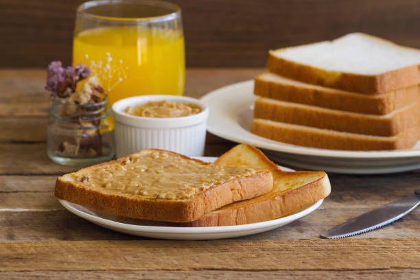 Toast bread with homemade peanut butter served with orange juice. Homemade toast bread with peanut butter on wood table for breakfast.Delicious toast bread with homemade peanut butter ready to served.