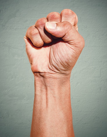 Riot protest fist raised in the air. Male clenched fist on dark grunge background.