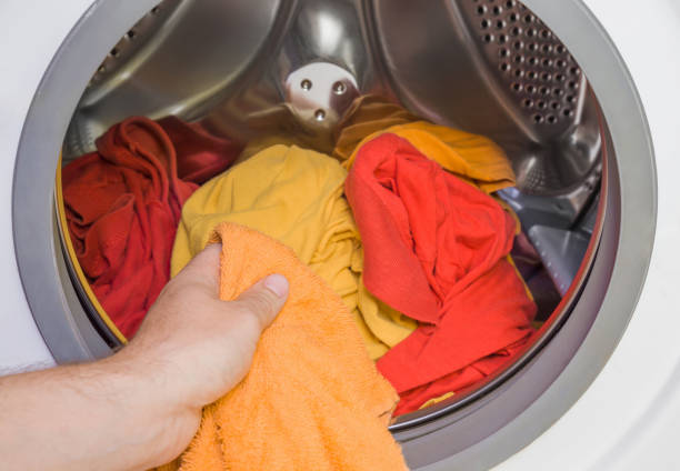 istock Husband's hand loading full washing machine with colorful clothes. Dry cleaning concept. Clothes care. Regular washing. 842427846