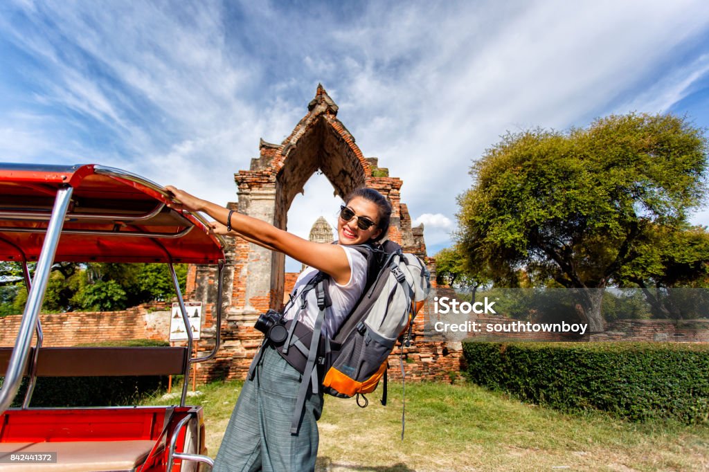 Young asian female traveler with backpack traveling with standing on taxi or Tuk Tuk and happy fun with old temple (Wat Mahathat) background, Ayutthaya Province, Thailand Thailand Stock Photo
