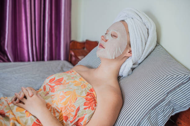 istock Young red-haired woman relaxing on a bed. Sheet mask on her face 842449508