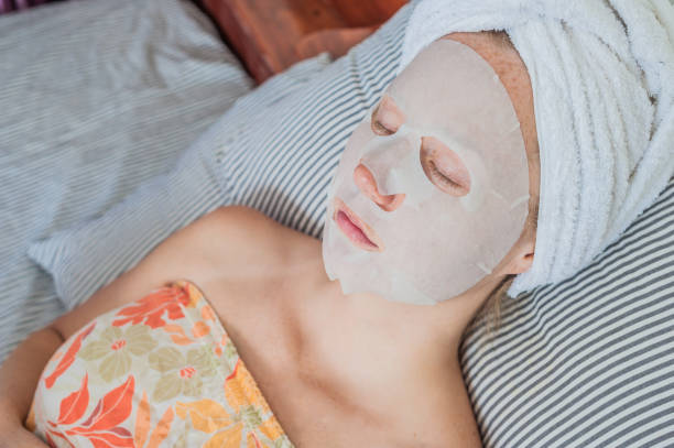 istock Young red-haired woman relaxing on a bed. Sheet mask on her face 842449516