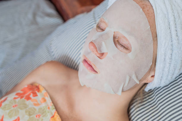 istock Young red-haired woman relaxing on a bed. Sheet mask on her face 842449556