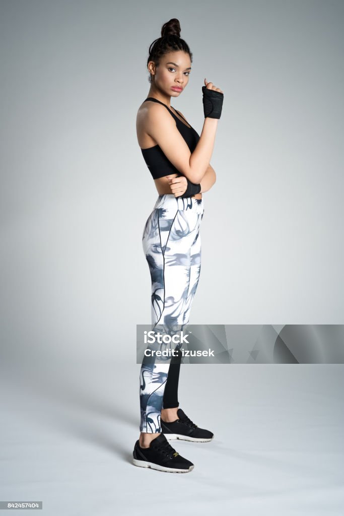 Side view of afro american young woman in sports wear, studio shot Full length of attractive young woman in sports wear standing against grey background, studio shot. 16-17 Years Stock Photo