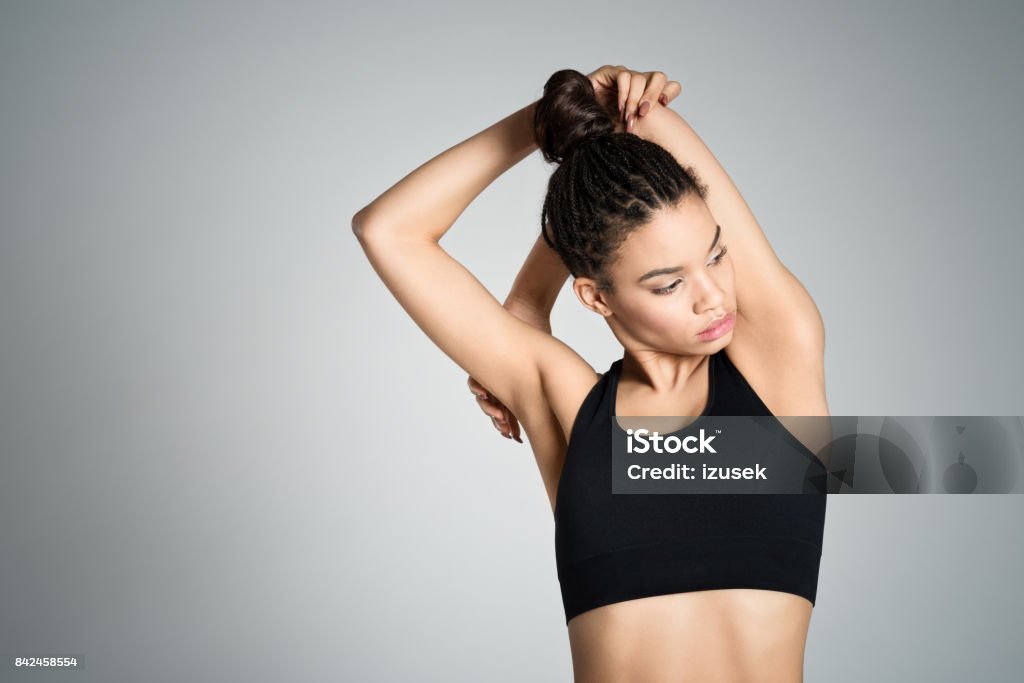Attractive fit young woman stretching her arms Attractive fit young woman restign after workout, stretching her arms. Studio shot, grey background. Arms Raised Stock Photo
