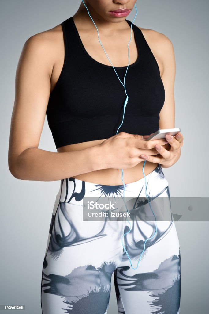 Fitness young woman using smart phone, studio shot Afro american young woman in sports wear using smart phone. Studio shot, grey background. 16-17 Years Stock Photo