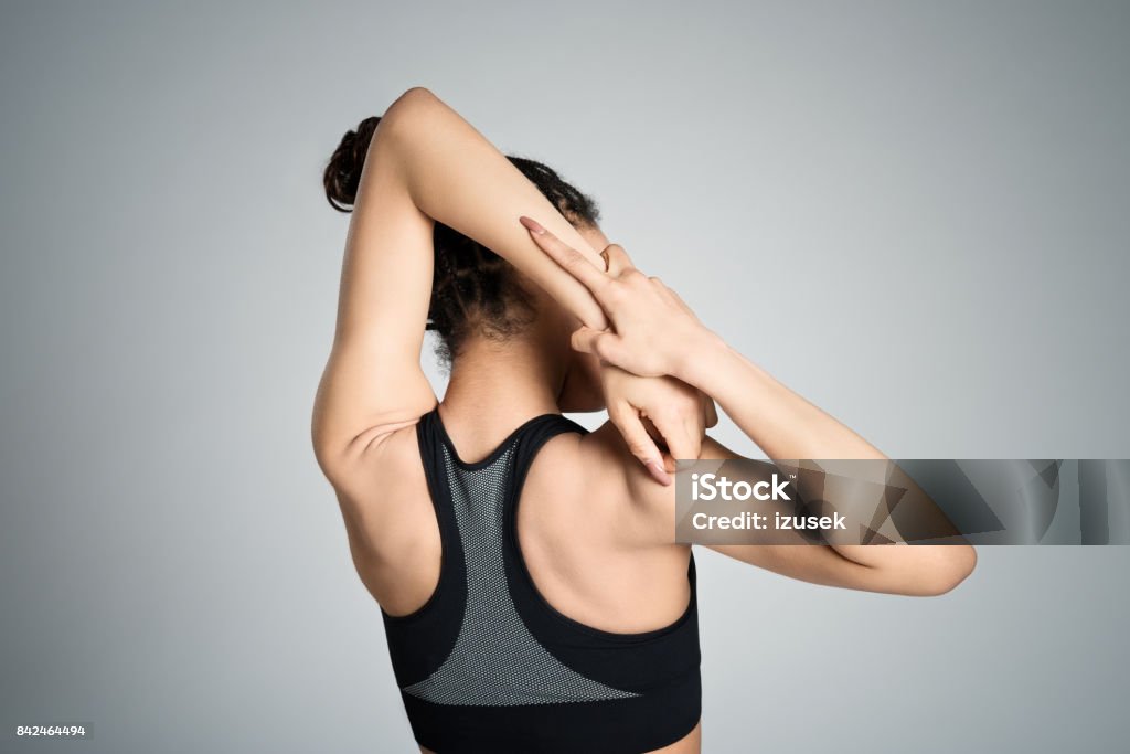 Back view of young woman stretching her arms Back view of fit young woman restign after workout, stretching her arms. Studio shot, grey background. 16-17 Years Stock Photo